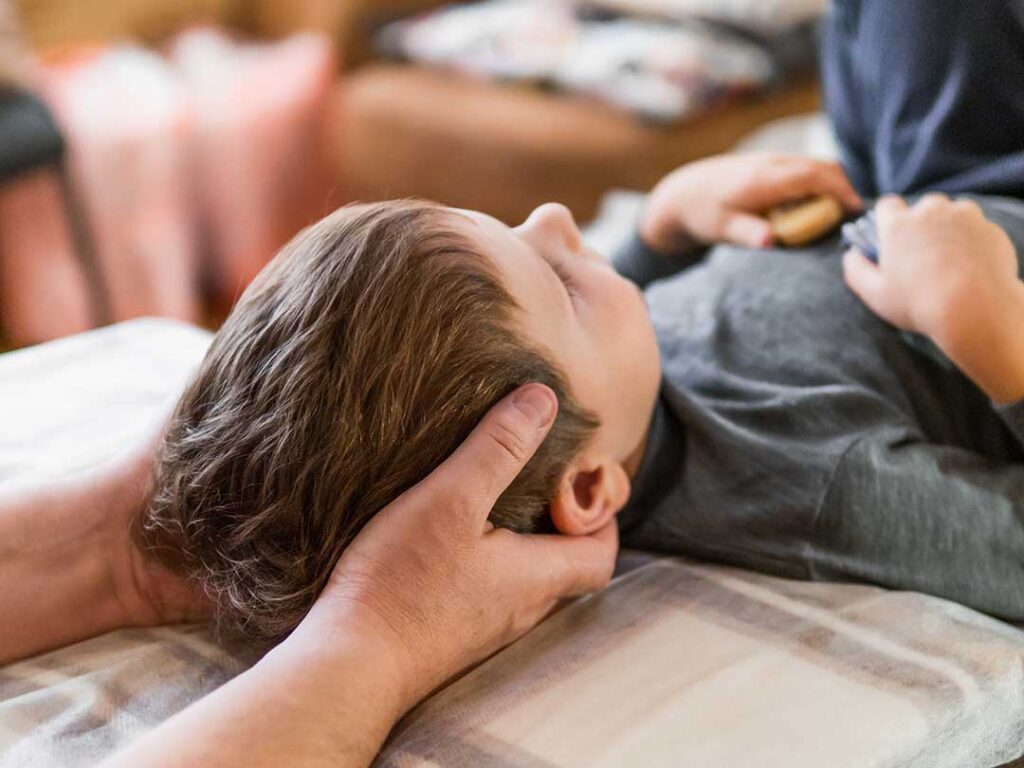 A person sits on an exam table while a healthcare provider gently examines their mid-back.