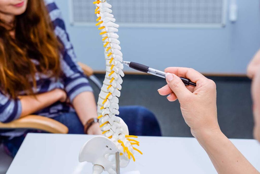 A clinician discusses movement with an adult beside an examination table in a bright wellness room.